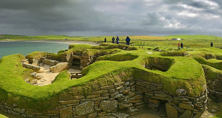 Ruines du village néolithique de Skara Brae recouvertes d'un gazon d'un vert éclatant à côté de la mer.