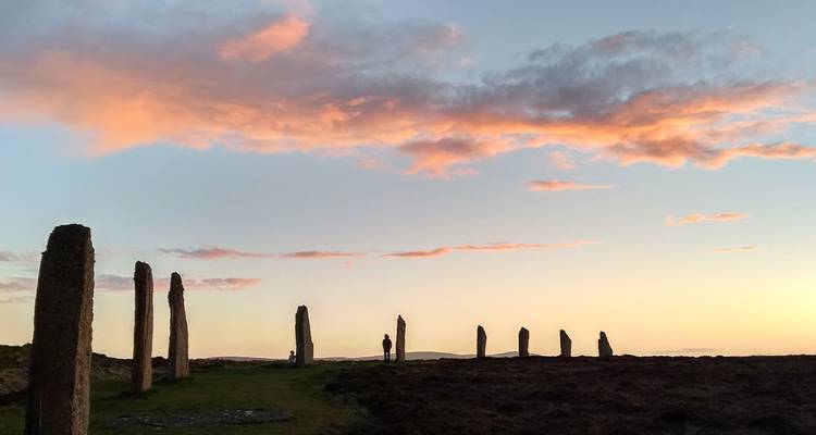 Les silhouettes des pierres levées de Stenness se détachant sur un ciel de coucher de soleil aux teintes pastel.