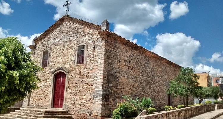 La même église en pierre rustique sous un ciel bleu avec des nuages épars.