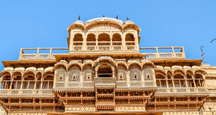 Voorkant van een haveli in Jaisalmer met ingewikkelde zandsteensculpturen die schitteren onder een strakblauwe hemel.