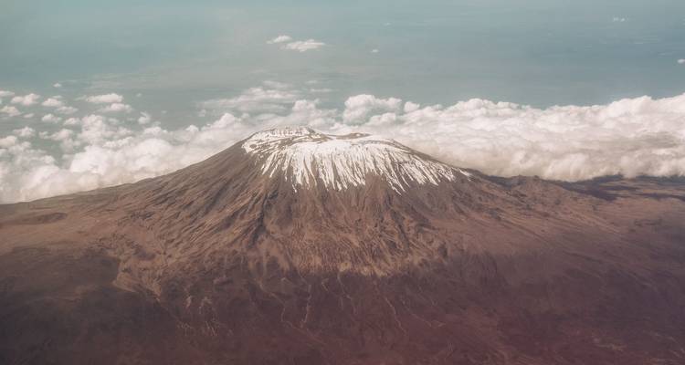 Aerial perspective of Kilimanjaro summit poking through cloud layer with snowy crater rim.