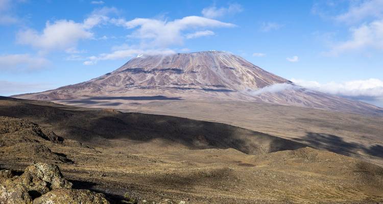 Crater peak of Kilimanjaro rises above barren high-altitude desert under bright sky.