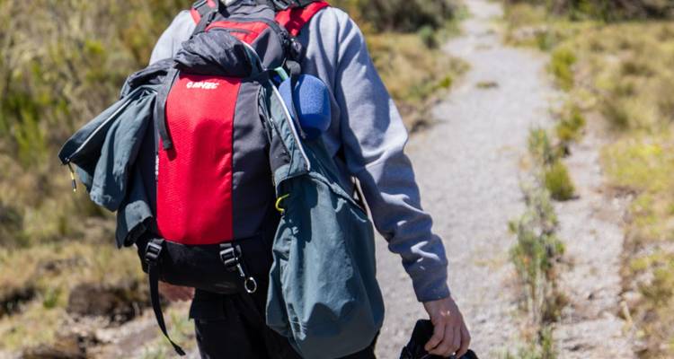Close-up of trekker carrying large backpack and camera while walking dusty alpine trail.