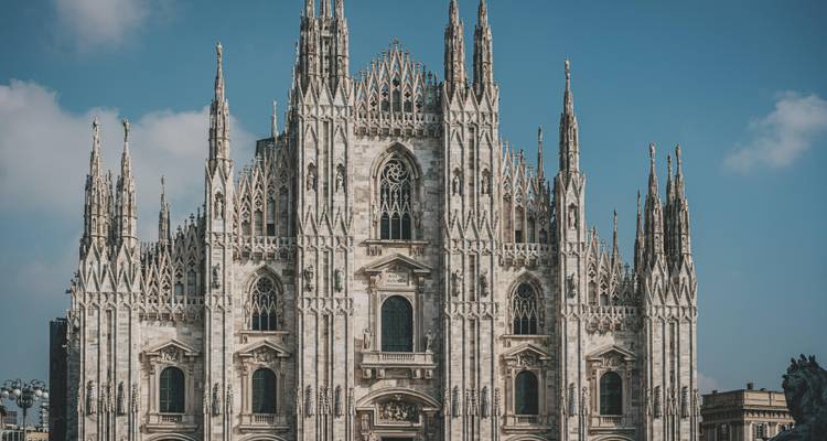 Front façade of Milan's ornate Gothic Duomo against a bright blue sky.
