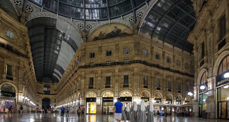 Night view inside Galleria Vittorio Emanuele II with shoppers beneath its glass-arched roof.