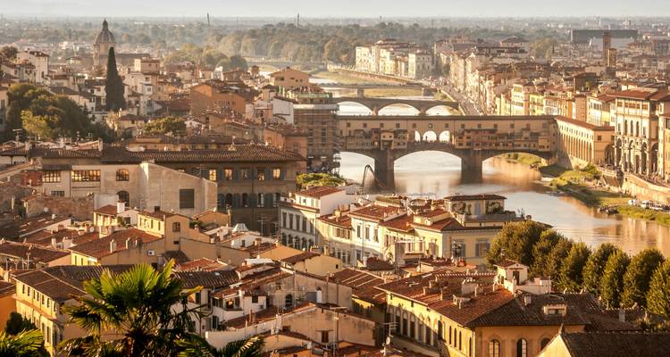 Warm evening light bathes Florence's Ponte Vecchio and the Arno River.