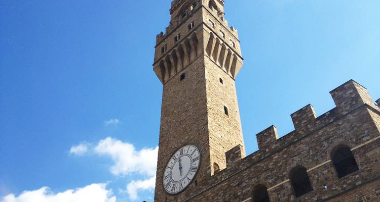 Stone clock tower of Palazzo Vecchio set against a bright blue sky.