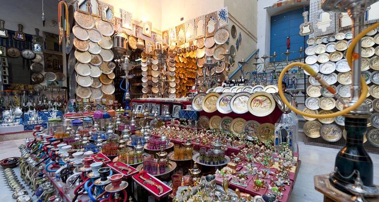 Une boutique intérieure de souk marocain remplie d'assiettes colorées, de narguilés, de parfums et d'artisanats traditionnels.