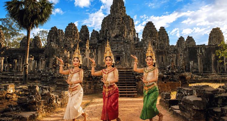 Three traditional Apsara dancers in ornate costumes perform before the stone towers of Bayon Temple.