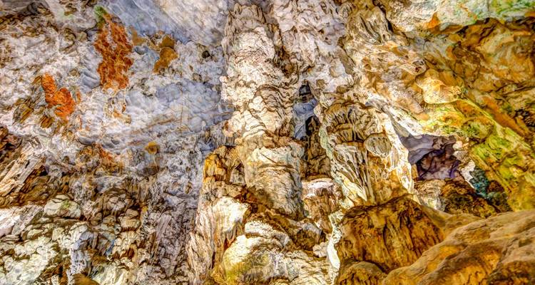 Colourful, illuminated limestone cave ceiling with dramatic stalactites and mineral formations
