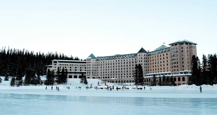L'hôtel Chateau Lake Louise surplombe les patineurs glissant sur un vaste lac gelé entouré de sapins.
