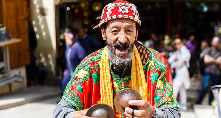 Traditional Moroccan street musician in colourful attire joyfully playing metal castanets.