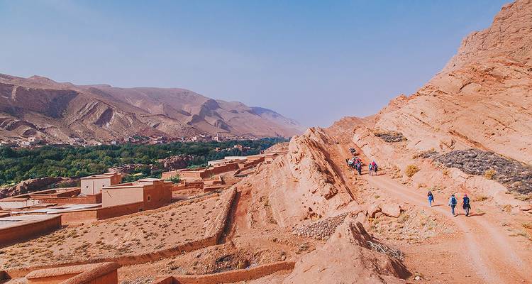 Les randonneurs cheminent le long d'une crête poussiéreuse surplombant une vallée luxuriante et les contreforts accidentés de l'Atlas.