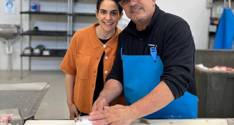 Deux poisonniers posent joyeusement en filetant du poisson frais sur un comptoir en acier inoxydable dans un marché de fruits de mer.