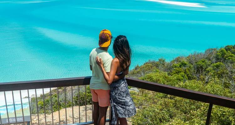 Una pareja se abraza mientras contemplan las brillantes aguas turquesas desde un balcón de madera en Hill Inlet.