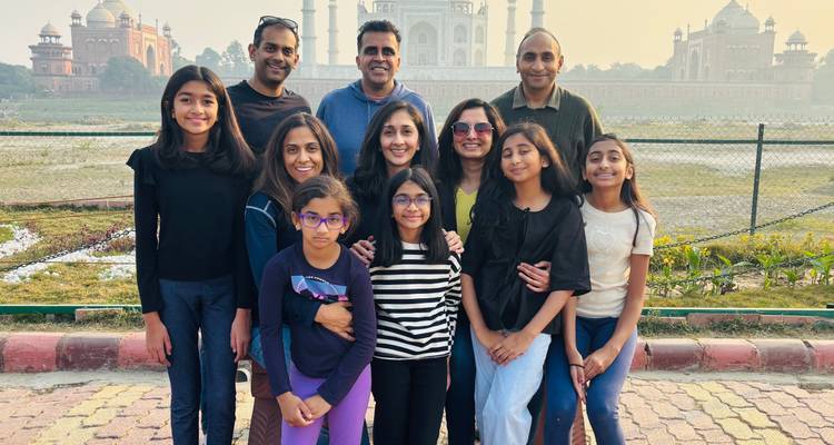 Extended family poses together with the Taj Mahal softly visible through morning haze.