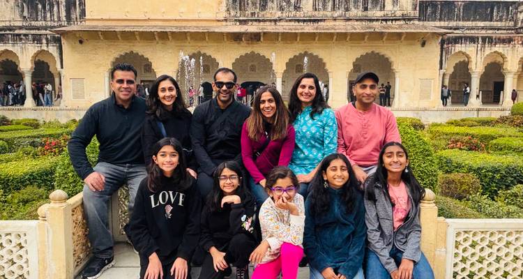 Large family group sits on a stone bench in front of an historic Indian palace courtyard.
