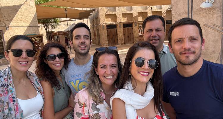 Friends take a cheerful close-up selfie under shade sails in a rustic market setting.