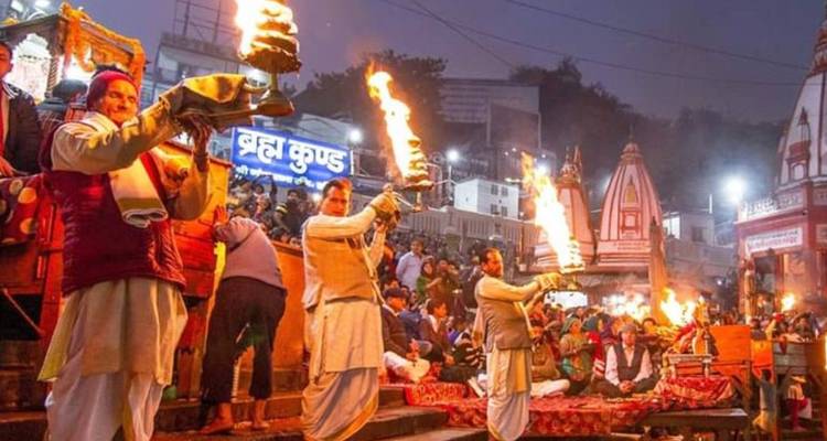 Evening Ganga Aarti in Haridwar with priests holding giant flame lamps before a dense crowd.