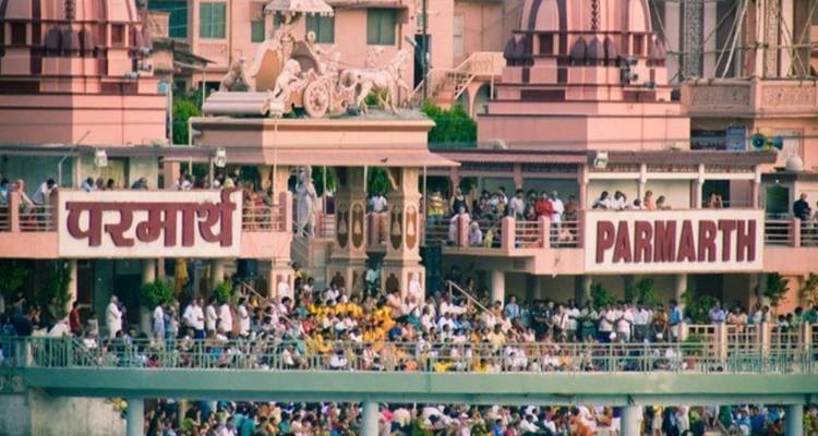 Crowds gather outside Parmarth Niketan Ashram complex with large Hindi signage.