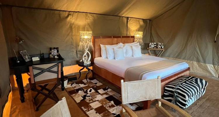Luxurious safari tent interior with neatly made double bed, designer lamps and animal-print decor.