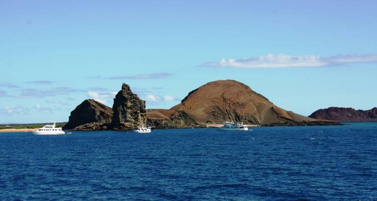 Distant volcanic islands emerging from the deep blue waters of the Galapagos archipelago with tour boats nearby.