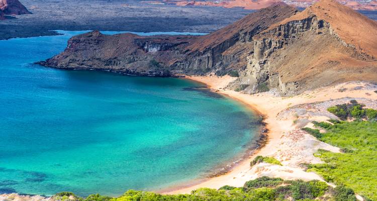 Sweeping view of a turquoise bay, golden beach and rugged volcanic slopes at Bartolomé Island in the Galapagos.