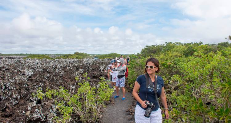 Tourists walking along a volcanic trail bordered by sparse shrubs and rugged lava formations.