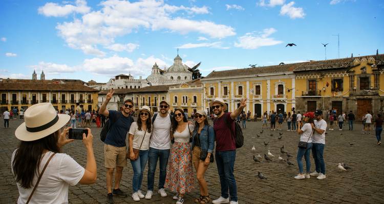 Group posing for a photo in Quito's historic square with pigeons and colonial buildings around.
