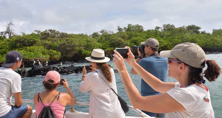 Passengers on a small boat photographing seabirds along a rocky Galapagos shoreline.