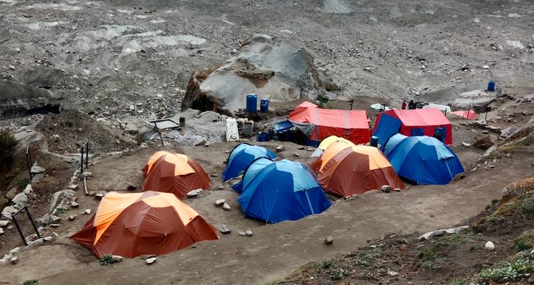 Rangée de tentes d'expédition aux couleurs vives dressées sur un site de camping en bordure de glacier rocheux.