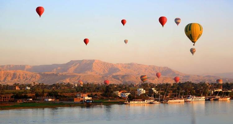 Hot-air balloons float above the Nile River with golden mountains lit by morning sun.