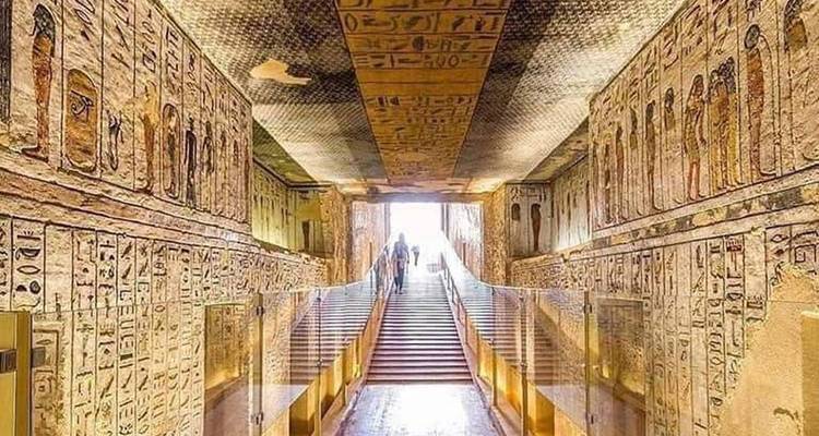 Colorful hieroglyph-covered corridor inside an ancient tomb with visitors descending the stairs.