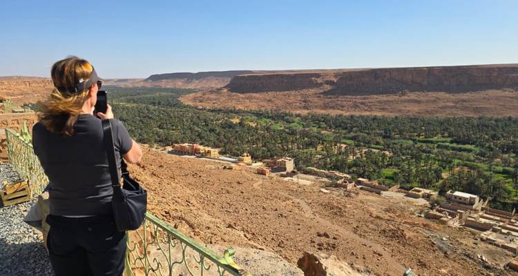 Un viajero sacando fotos de un oasis exuberante junto al río desde un mirador en lo alto de un acantilado en el sur de Marruecos.