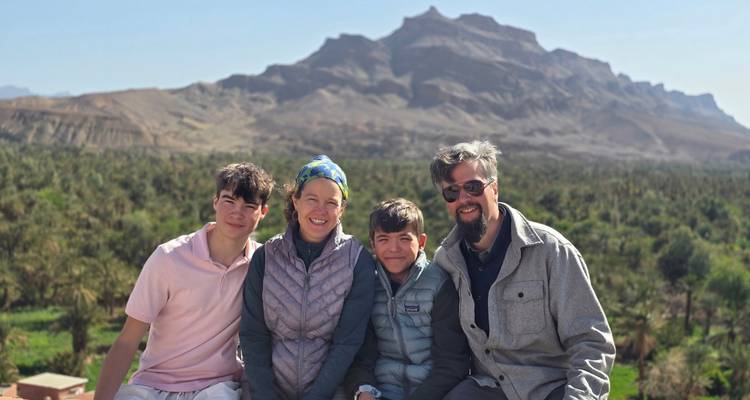 Familia sonriente de cuatro personas con un valle lleno de palmeras y escarpadas montañas de fondo.