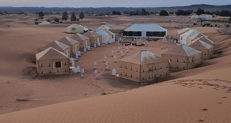 Campamento de tiendas de campaña organizado en filas ordenadas entre las infinitas dunas del Sahara al atardecer.