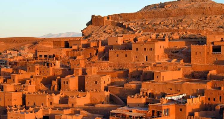 Pueblo de la kasbah de adobe brillando en naranja al atardecer en la cima de una colina desértica.