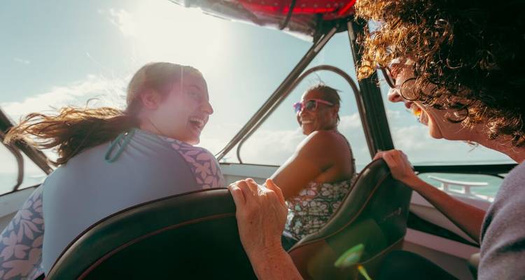 Friends laughing together on a speedboat with bright sun shining through the canopy.