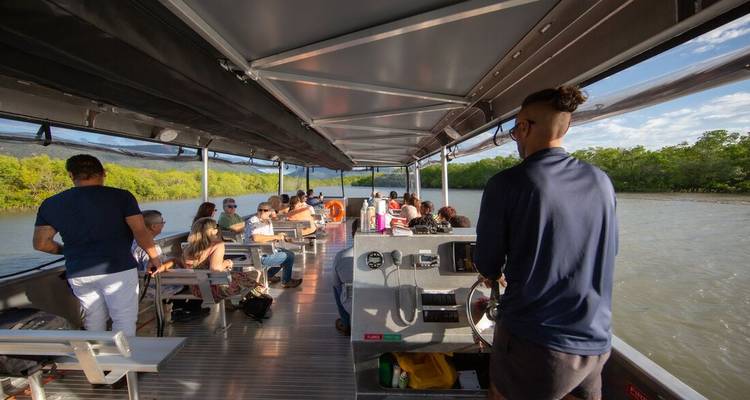 Passengers relax on an open-sided riverboat cruising along a mangrove-lined waterway.