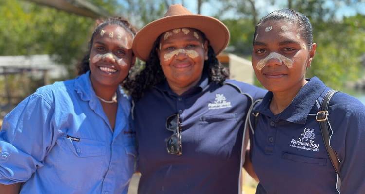 Three Indigenous women smiling with traditional face paint during a cultural experience.