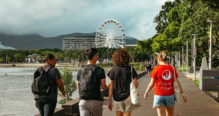 Les voyageurs se promènent le long de l'esplanade de Cairns avec la grande roue et les collines couvertes de forêt tropicale en arrière-plan.