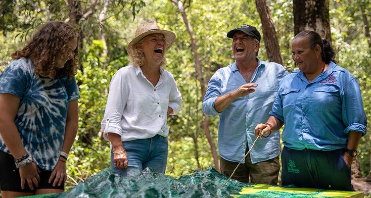 Les visiteurs rient aux côtés d'un guide autochtone qui présente un modèle topographique dans un cadre de forêt tropicale.