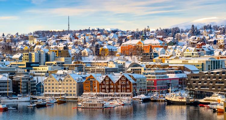 Bright winter panorama of Tromsø with colorful wooden houses, marina and snowy hillsides.