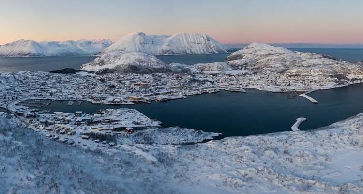 Aerial dusk view of snow-covered coastal town nestled among rugged islands and fjords.