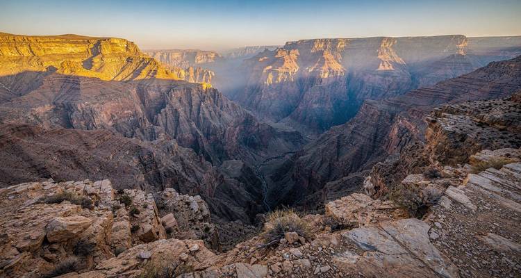 Vistas espectaculares del cañón en Jebel Shams con la luz dorada iluminando acantilados escarpados y gargantas profundas.