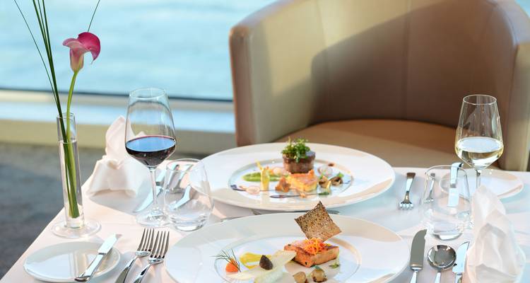 Comida gourmet de varios platos elegantemente presentada con copas de vino con vistas al agua.