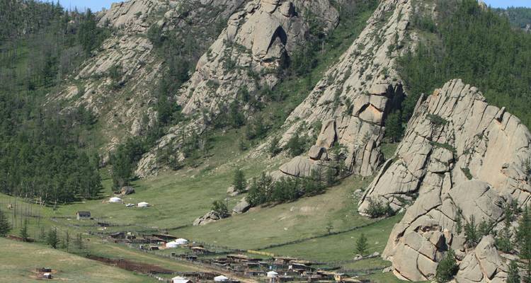 Rocky granite formations and scattered gers in a grassy Mongolian valley