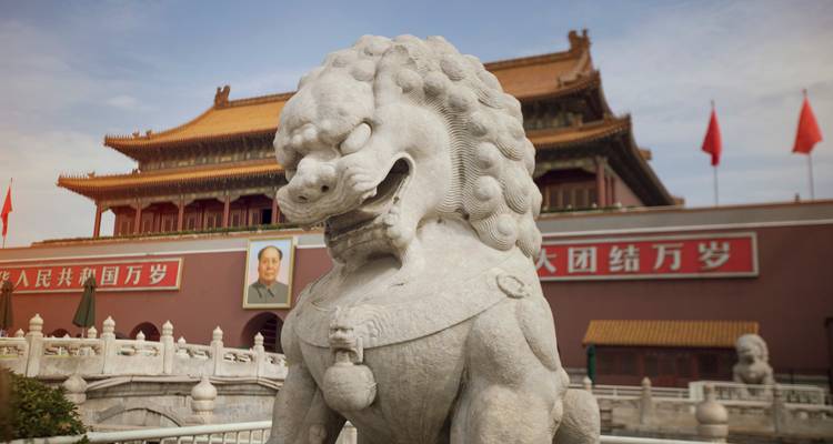 Estatua de león guardián de piedra con la Puerta de Tiananmen y el retrato de Mao de fondo