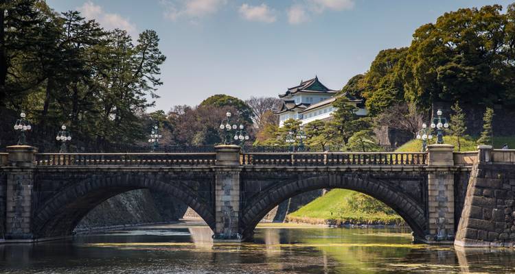 Elegant stone bridge spanning a moat with the Imperial Palace and lush greenery in the distance.