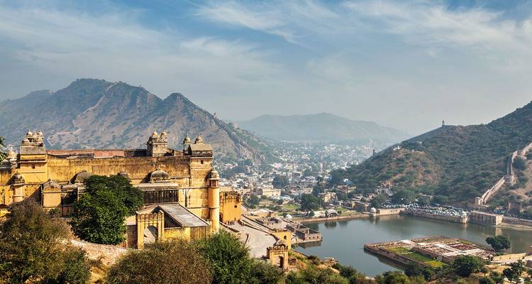 Vista panorámica del Fuerte Ámbar que domina un lago con colinas áridas y la ciudad de Jaipur a lo lejos bajo un cielo azul.